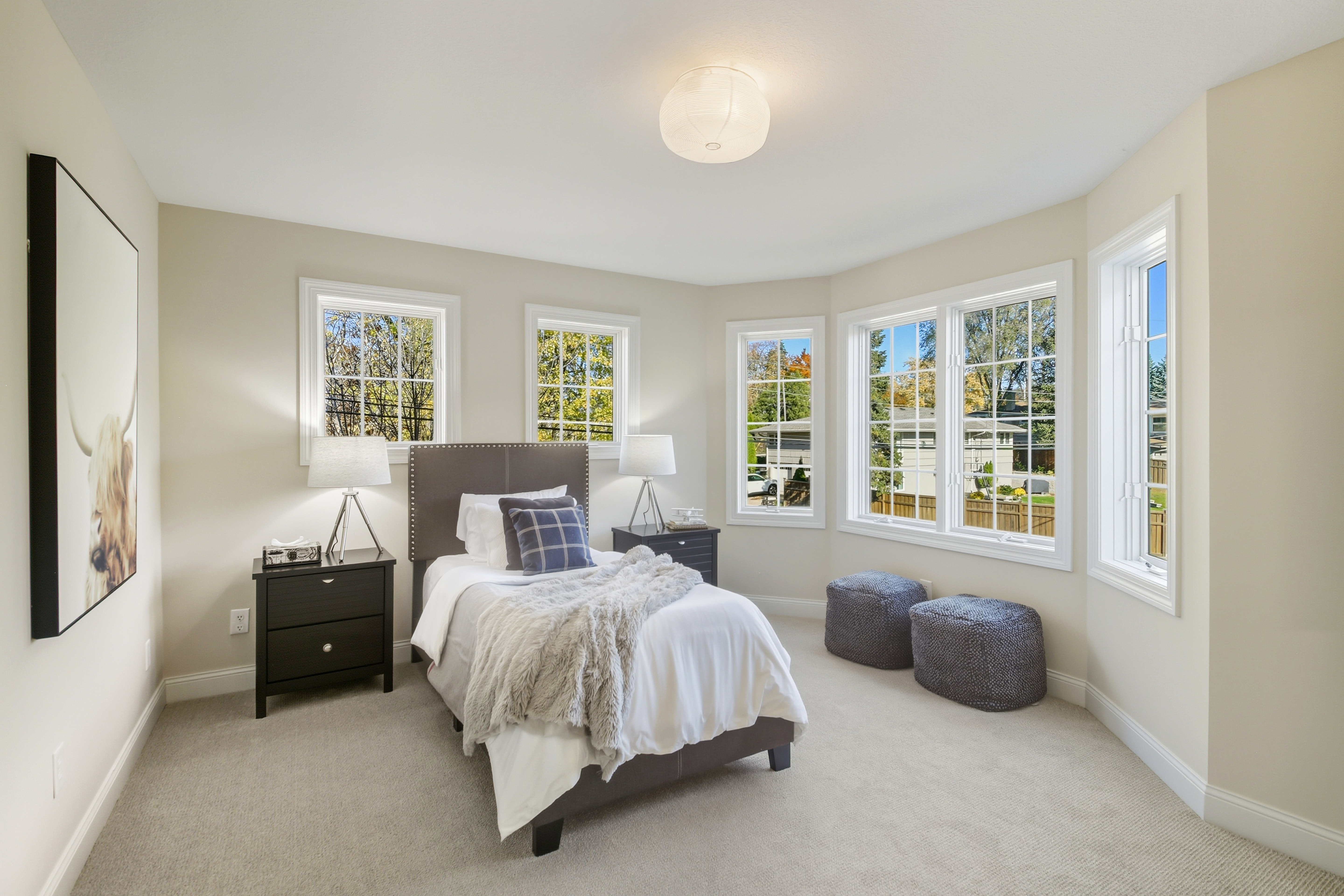 Modern two-story brick house with white garage doors, manicured lawn, and large windows surrounded by trees on a sunny day Modern two-story brick house with white garage doors, manicured lawn, and large windows surrounded by trees on a sunny day