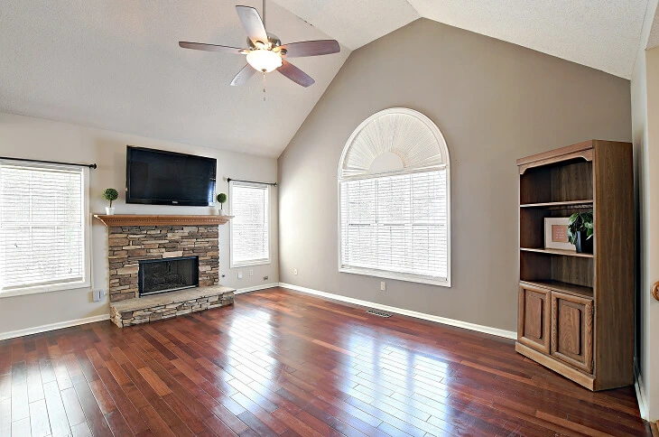 After photo of living room showing stone fireplace, vaulted ceiling, and dark wood floors, enhanced by Blue Dot Photos HDR editing.