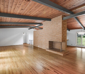 Empty living space with glossy hardwood floors, exposed wood beam ceiling, and a brick accent wall, ideal for unique listings.