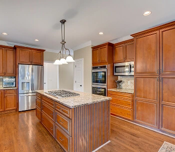 Kitchen interior with warm, traditional wood cabinets and a large center island with a cooktop, professionally photographed.