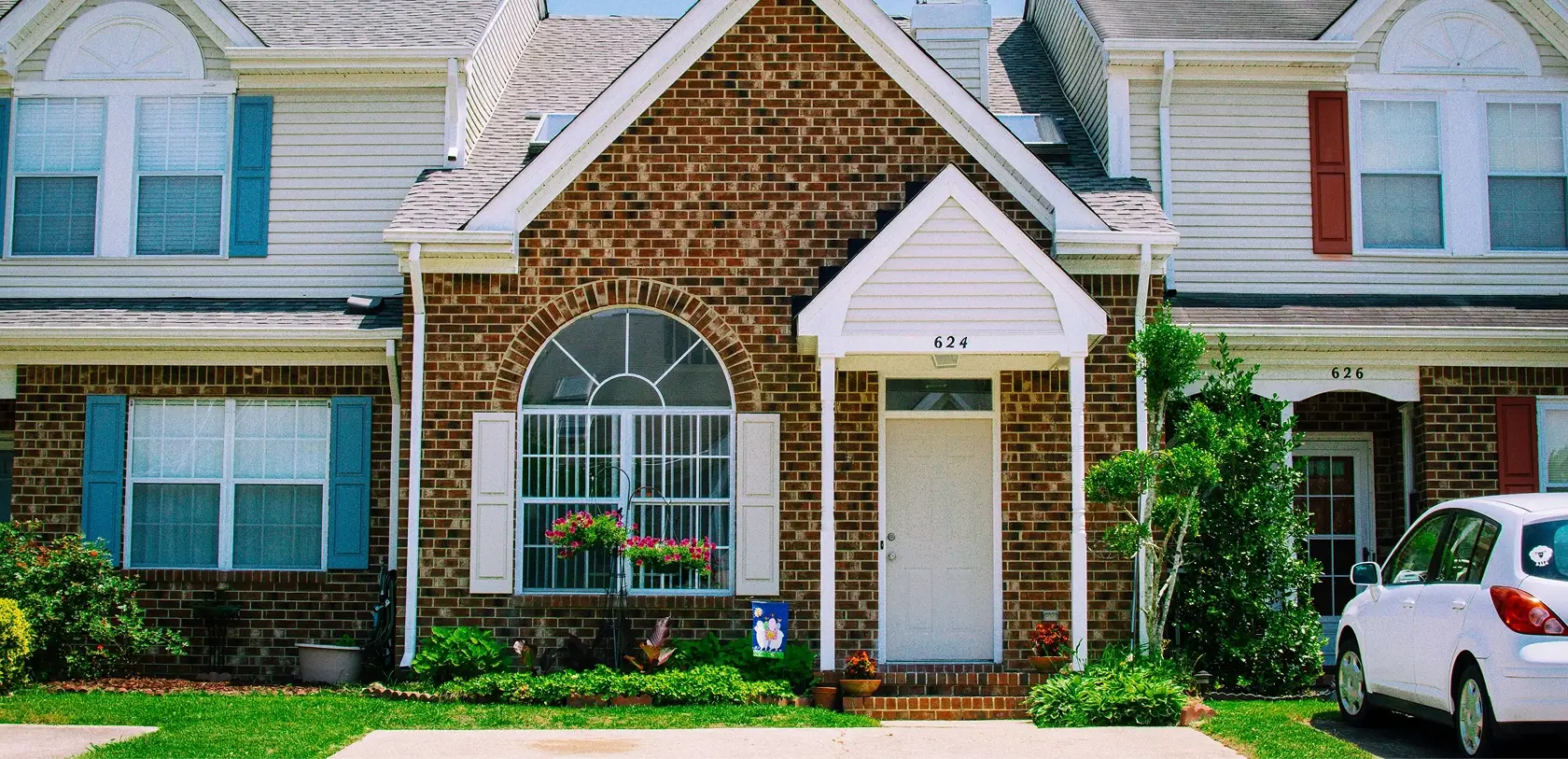 Traditional suburban home exterior with white siding, dark shutters, and a neatly maintained front lawn.