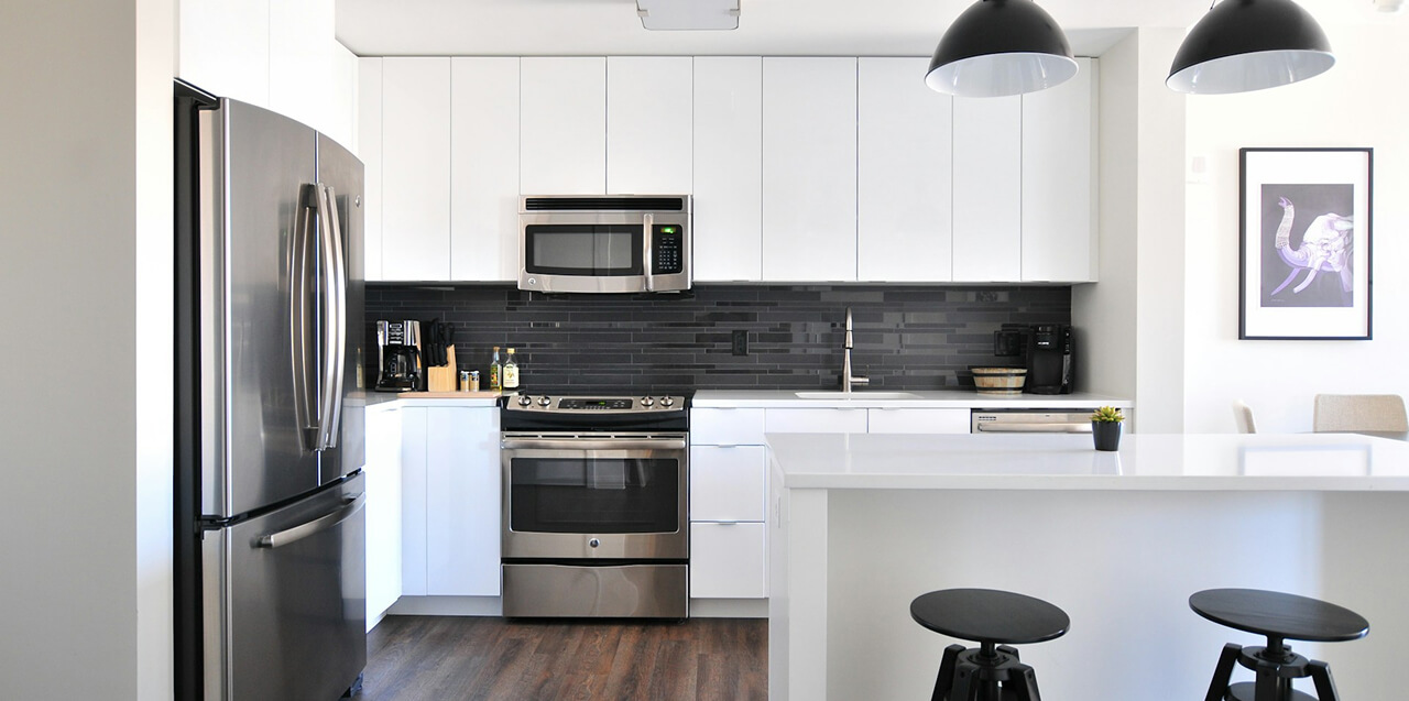 Minimalist kitchen interior with white subway tiles, open shelving, black light fixtures, and stainless-steel appliances.