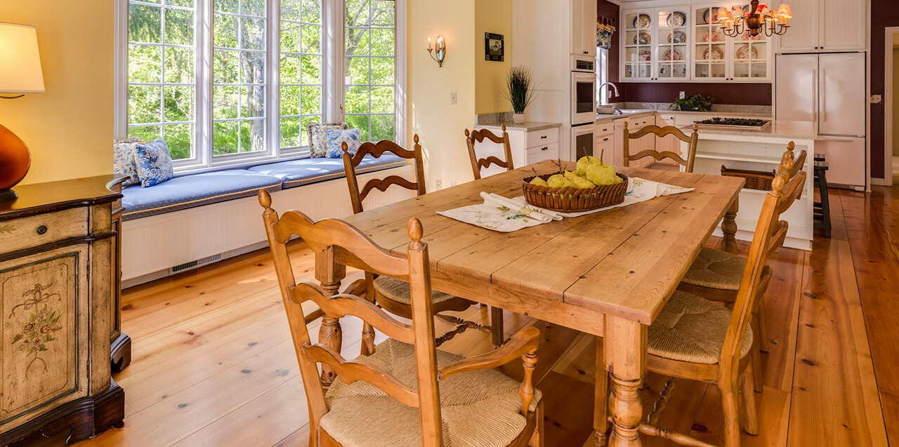 Dining room interior with a long rustic wooden table and chairs, photographed in natural light for a cozy, welcoming feel.