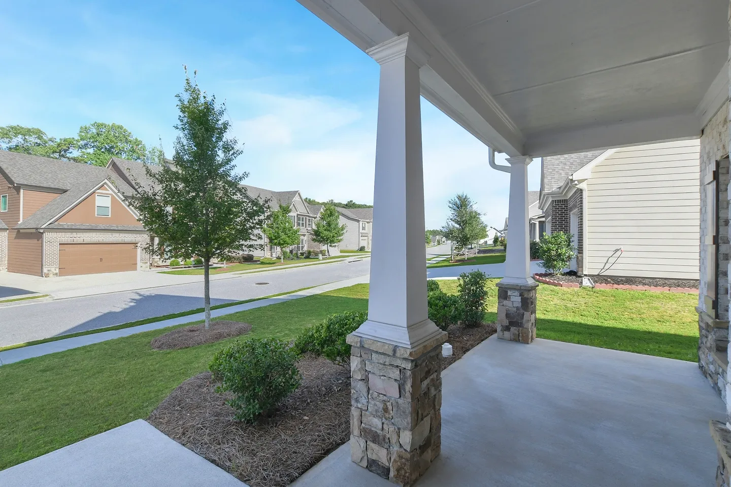Corner view of a covered front entryway, showing a stone path and manicured shrubs.