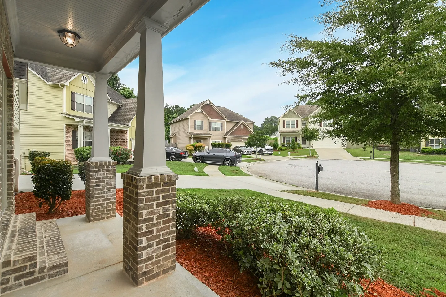 Close-up of a covered front porch entrance with columns, dark flooring, and mature landscaping.