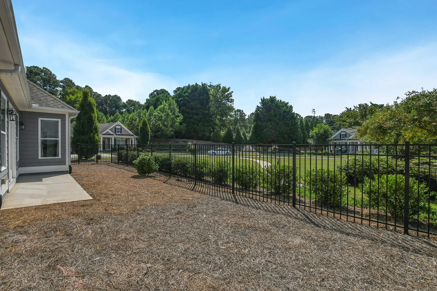 View across a large green backyard towards a distant house and a wooden privacy fence, showing full property size.