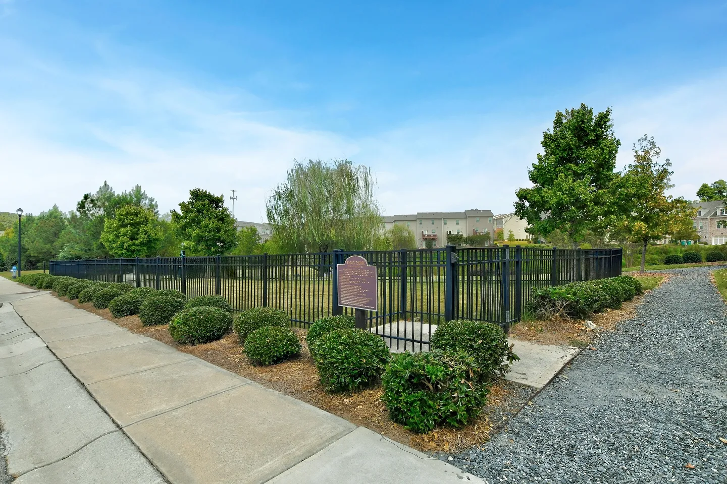 View of a manicured community sidewalk and green space with decorative landscaping and small trees.