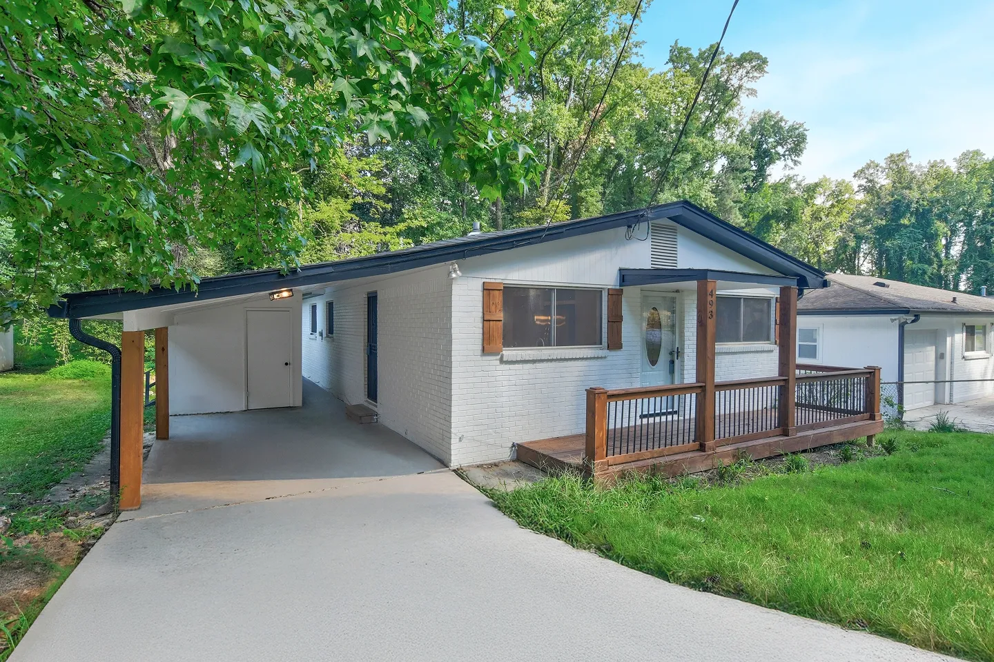 Single-story ranch-style home with white siding, covered entryway, and mature trees in the foreground.