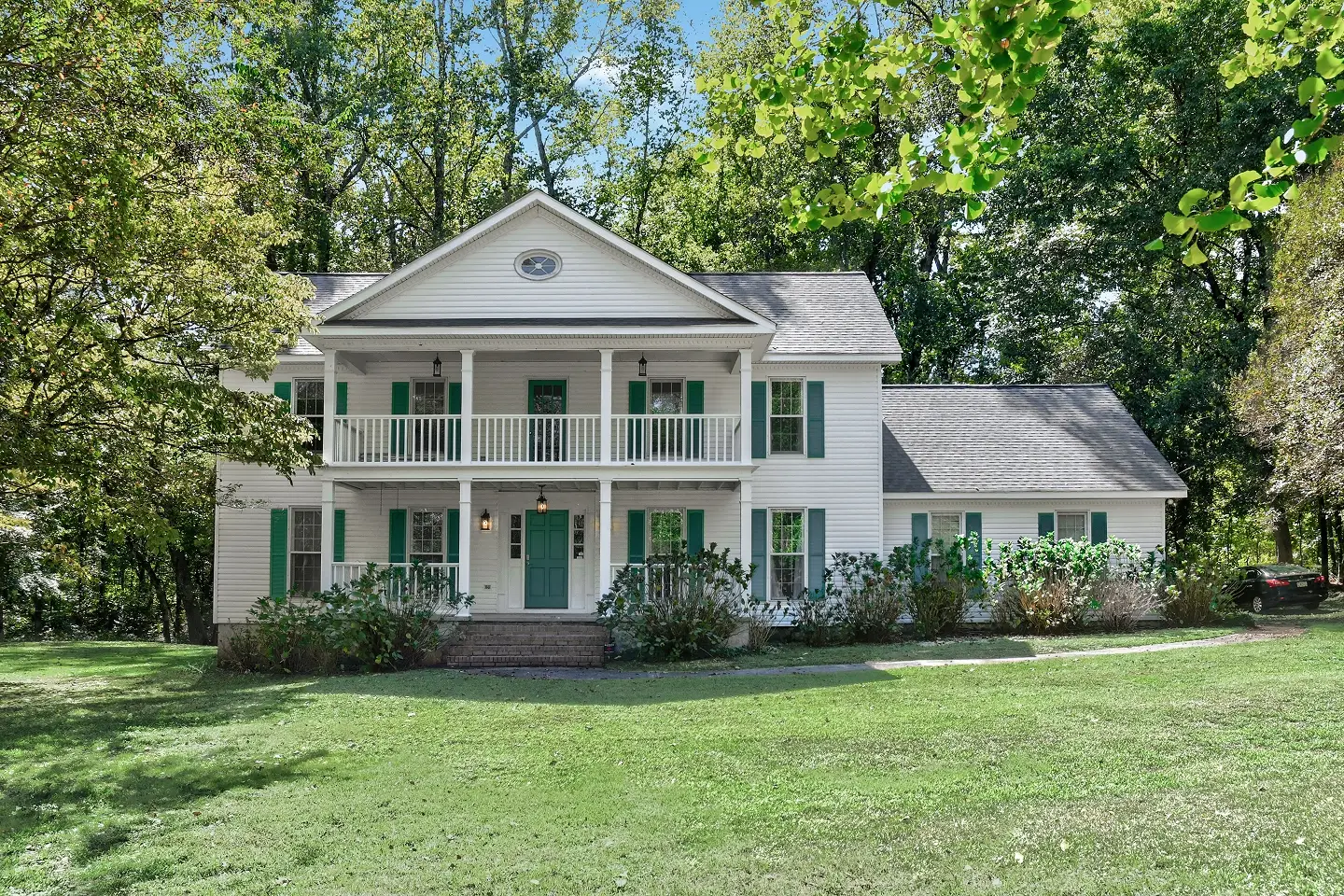 Traditional, two-story white house with dark shutters and a wide front porch, example of high-quality exterior real estate photography.