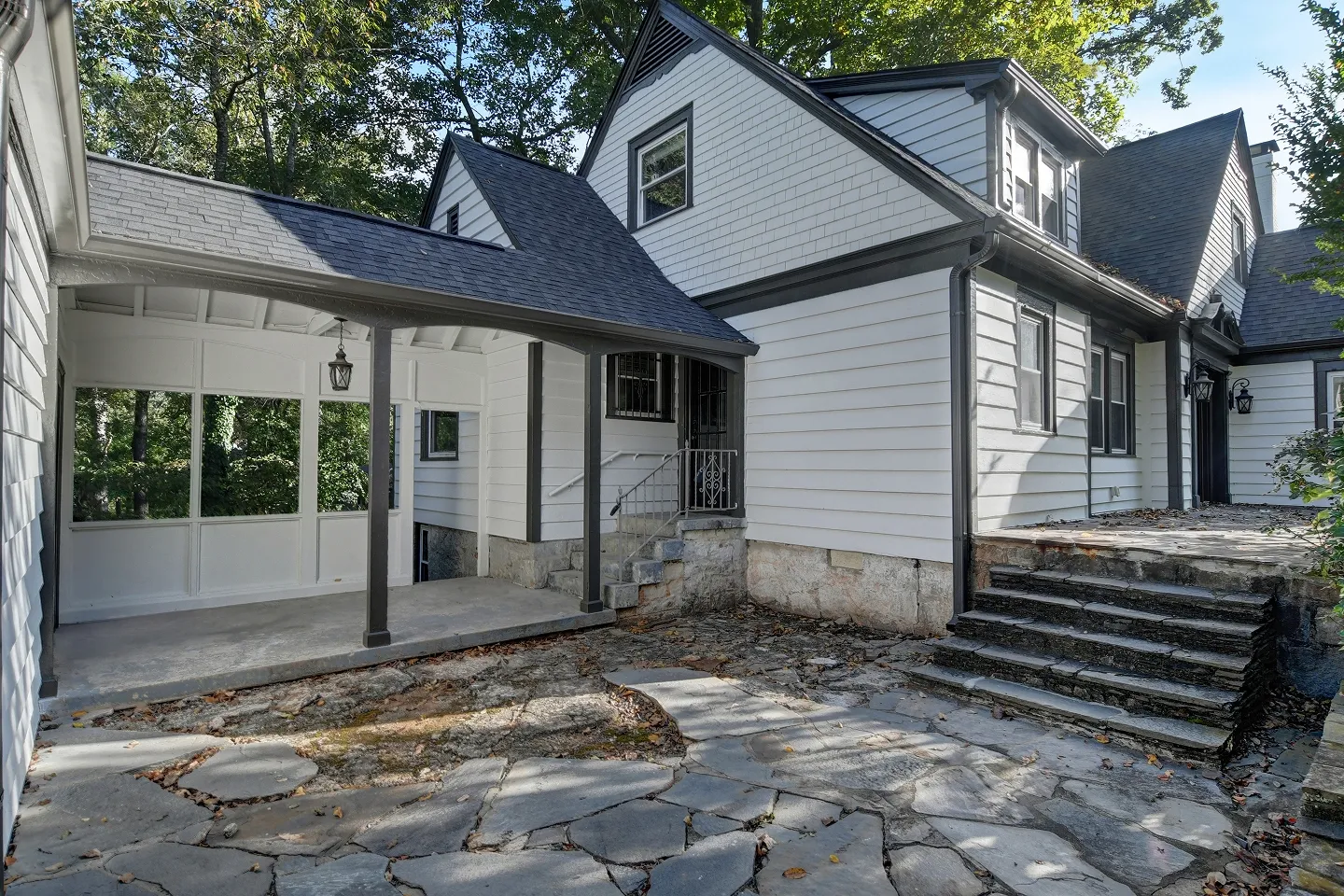 Side and back view of a white home with dark trim and stone landscaping leading to a patio area.