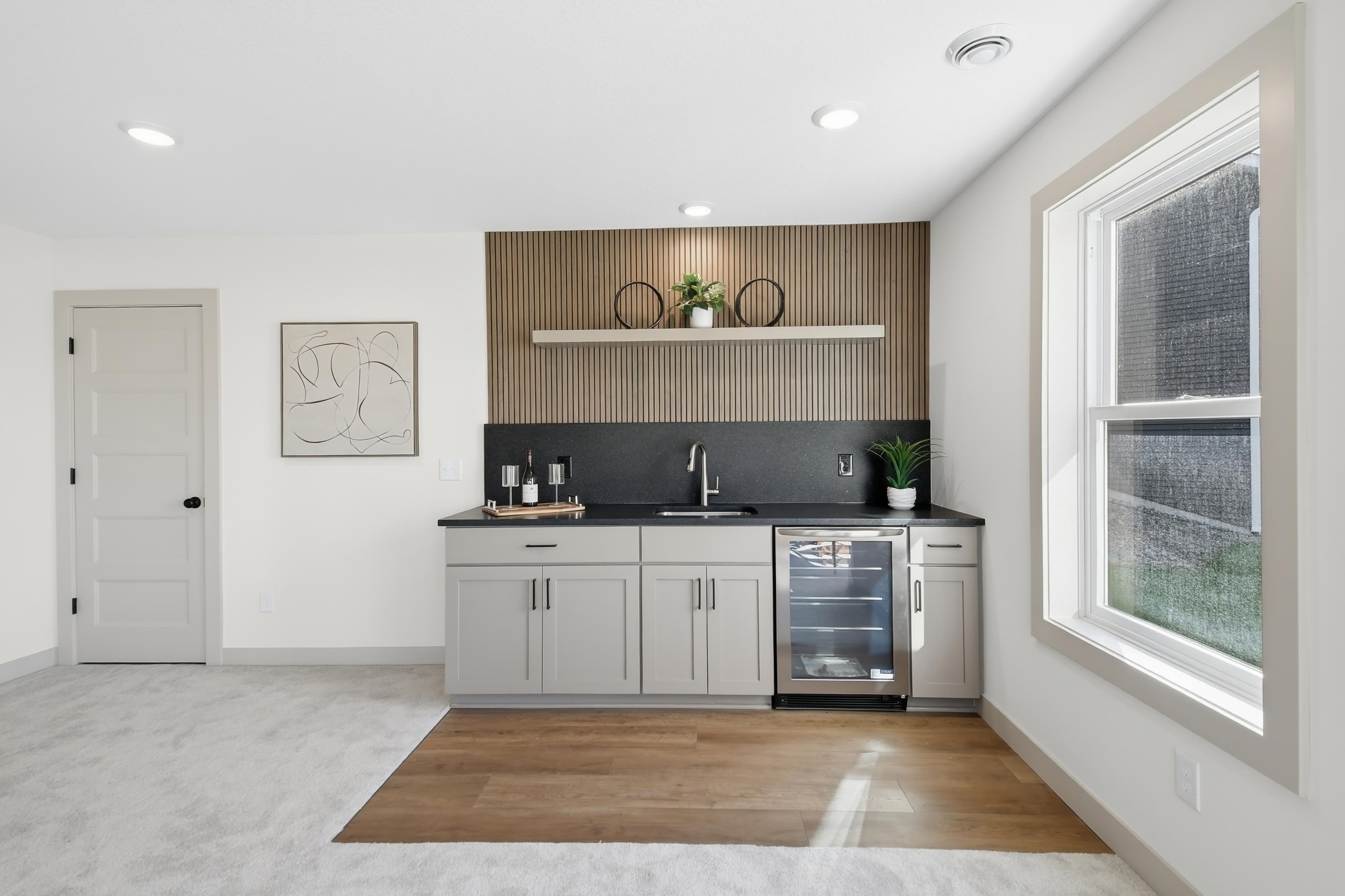 Lower-level wet bar with wood slat accent wall, black countertop, floating shelf, and beverage refrigerator