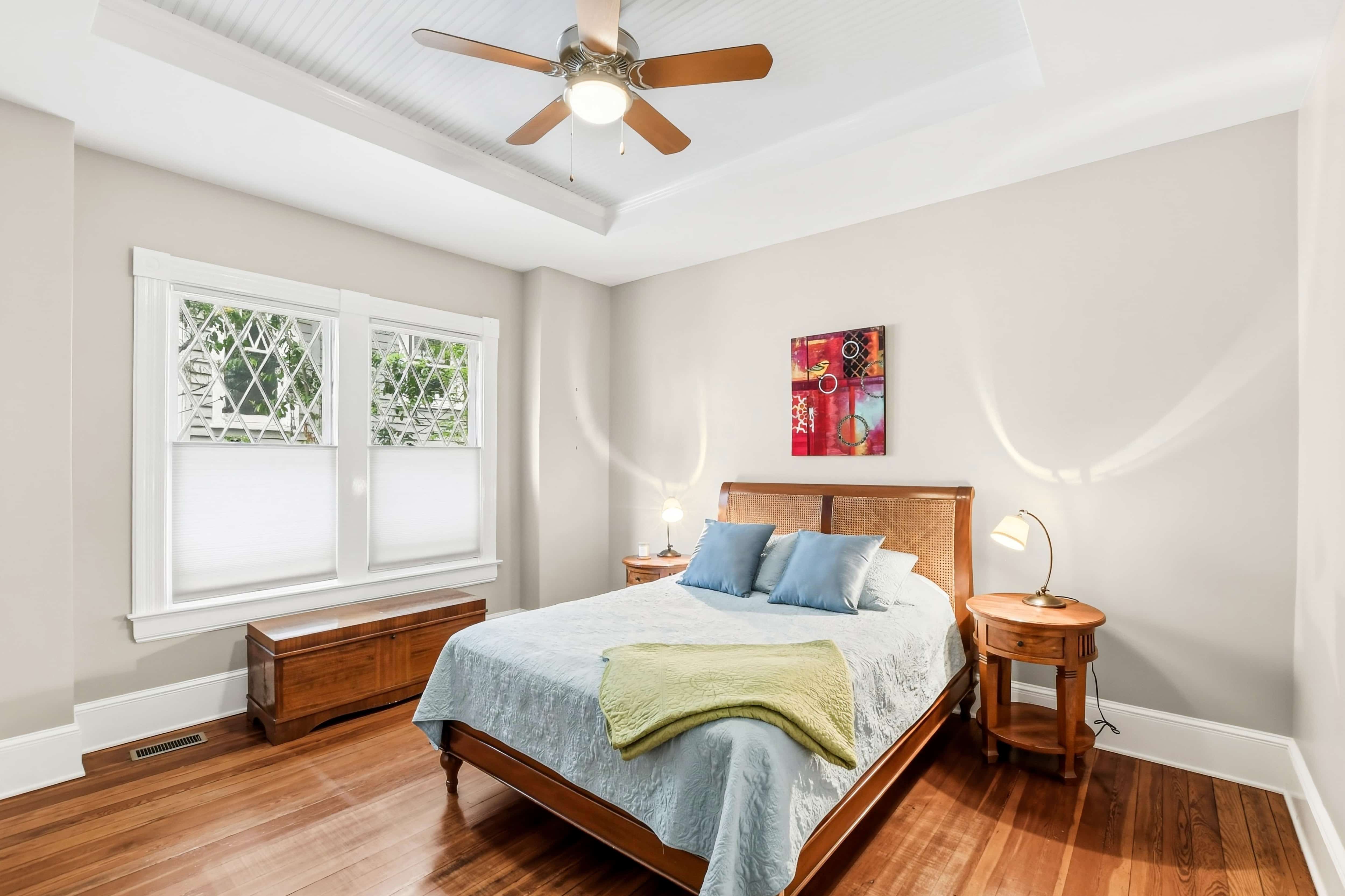 Bedroom with beadboard tray ceiling, leaded glass windows, ceiling fan, and hardwood floors