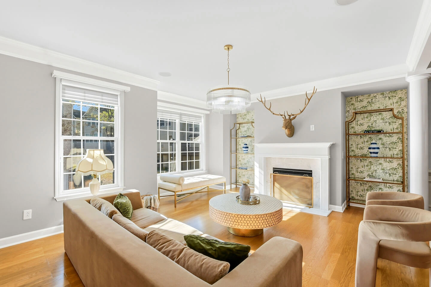 Living room with white fireplace, glass chandelier, wallpapered built-in shelves, and hardwood floors