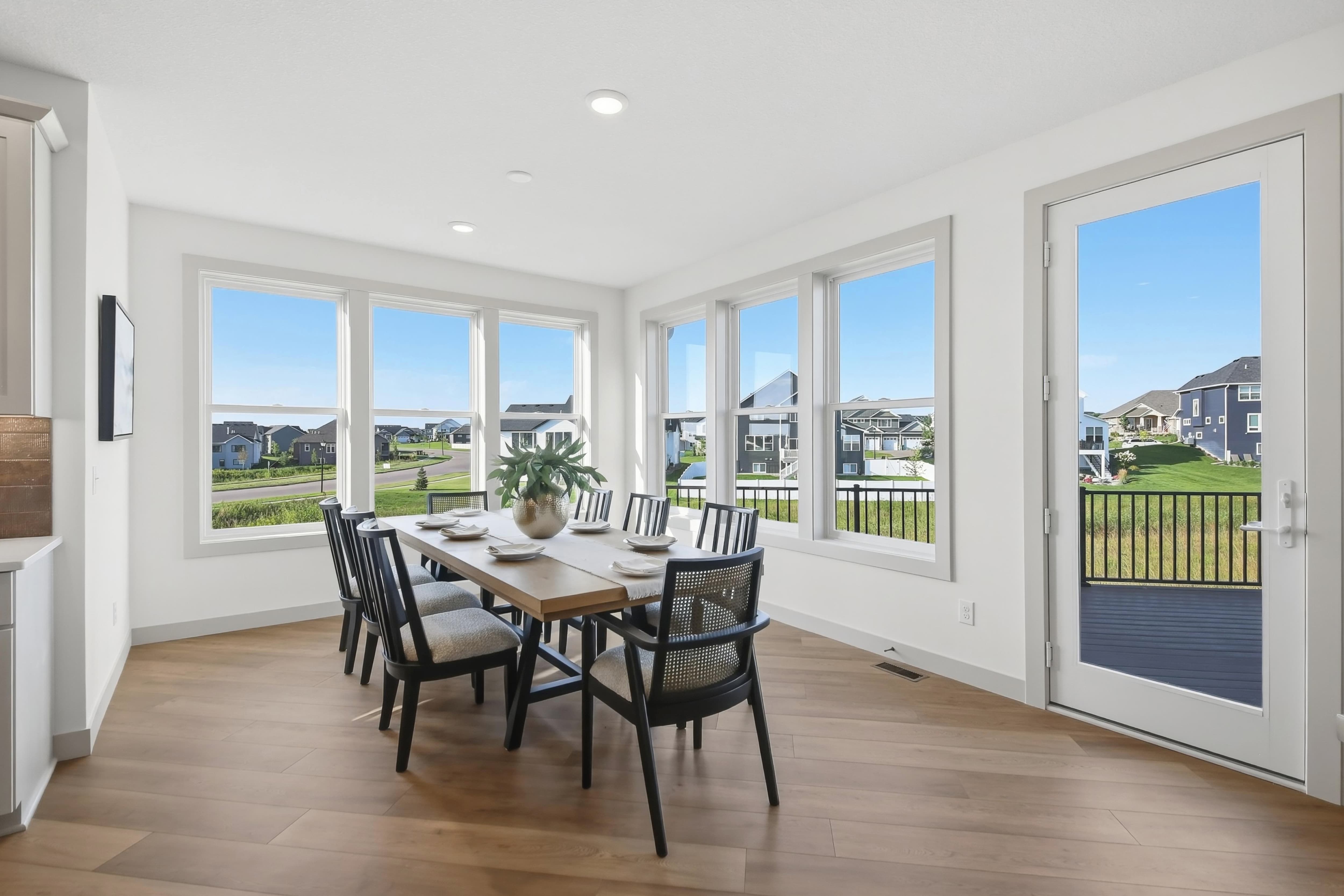 Bright dining area with a wall of windows, wood-look flooring, and a glass door leading to the deck
