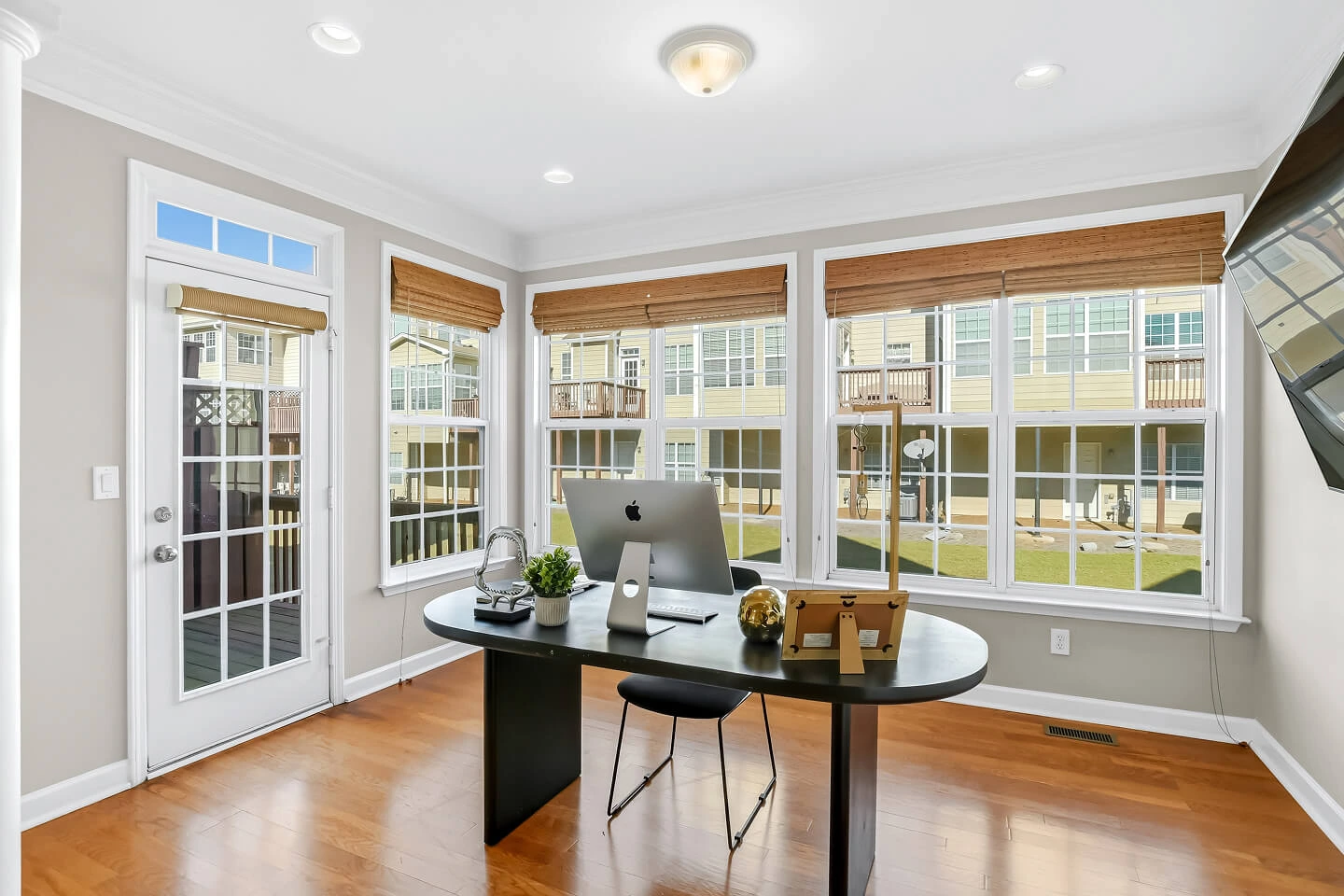 Home office with a wall of windows, woven shades, hardwood floors, and a glass door to the deck