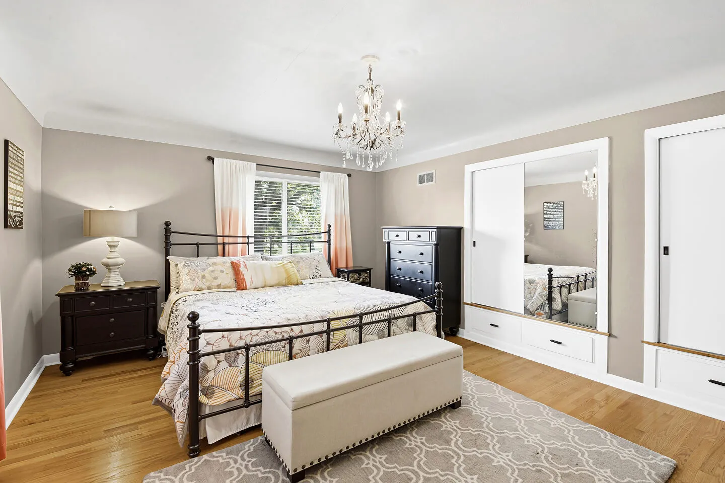 Bedroom with crystal chandelier, iron bed frame, hardwood floors, and built-in mirrored closets with drawers