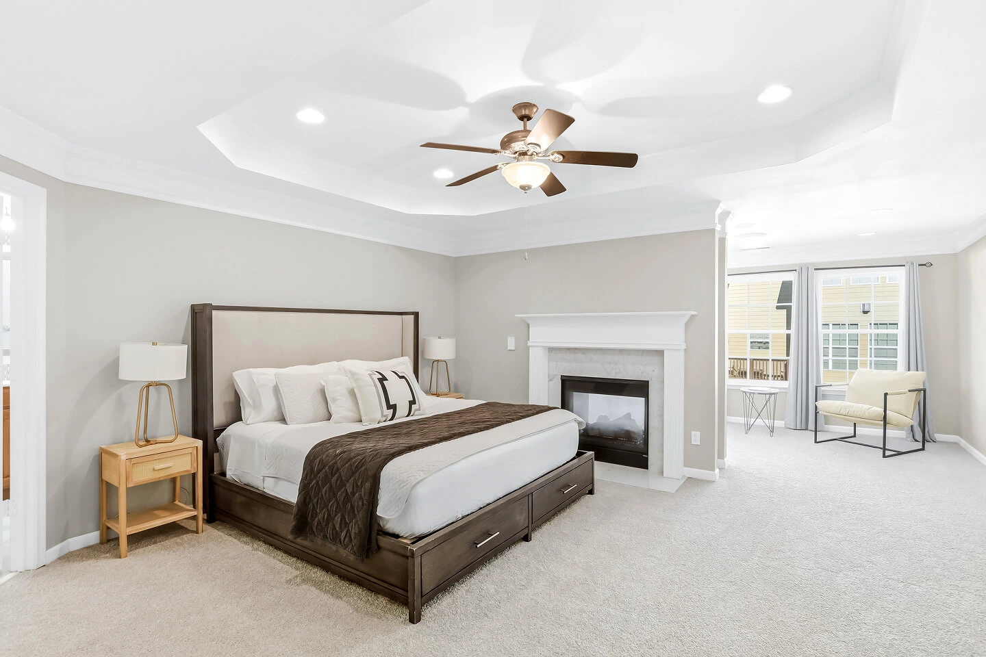 Primary bedroom with tray ceiling, fireplace, plush carpet, and a sitting area by the windows