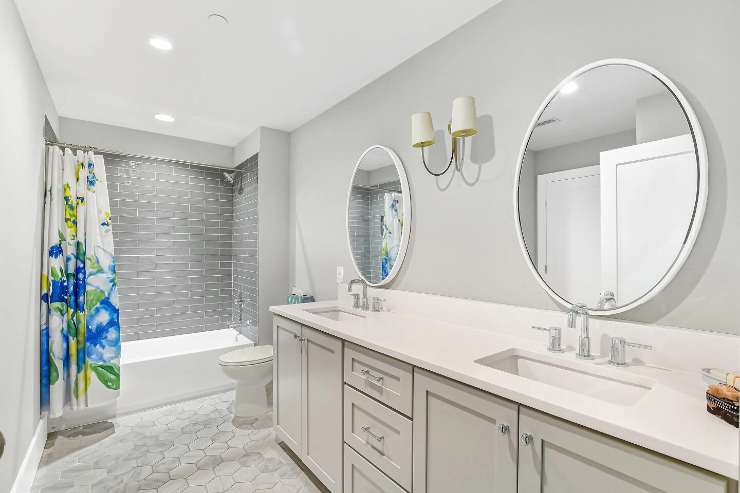 Bathroom with double sink vanity, round mirrors, hexagon tile floor, and gray subway tile tub surround