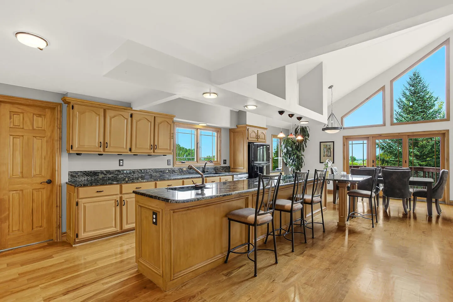 Open-concept kitchen with oak cabinets, granite island seating, and a dining area under a vaulted ceiling