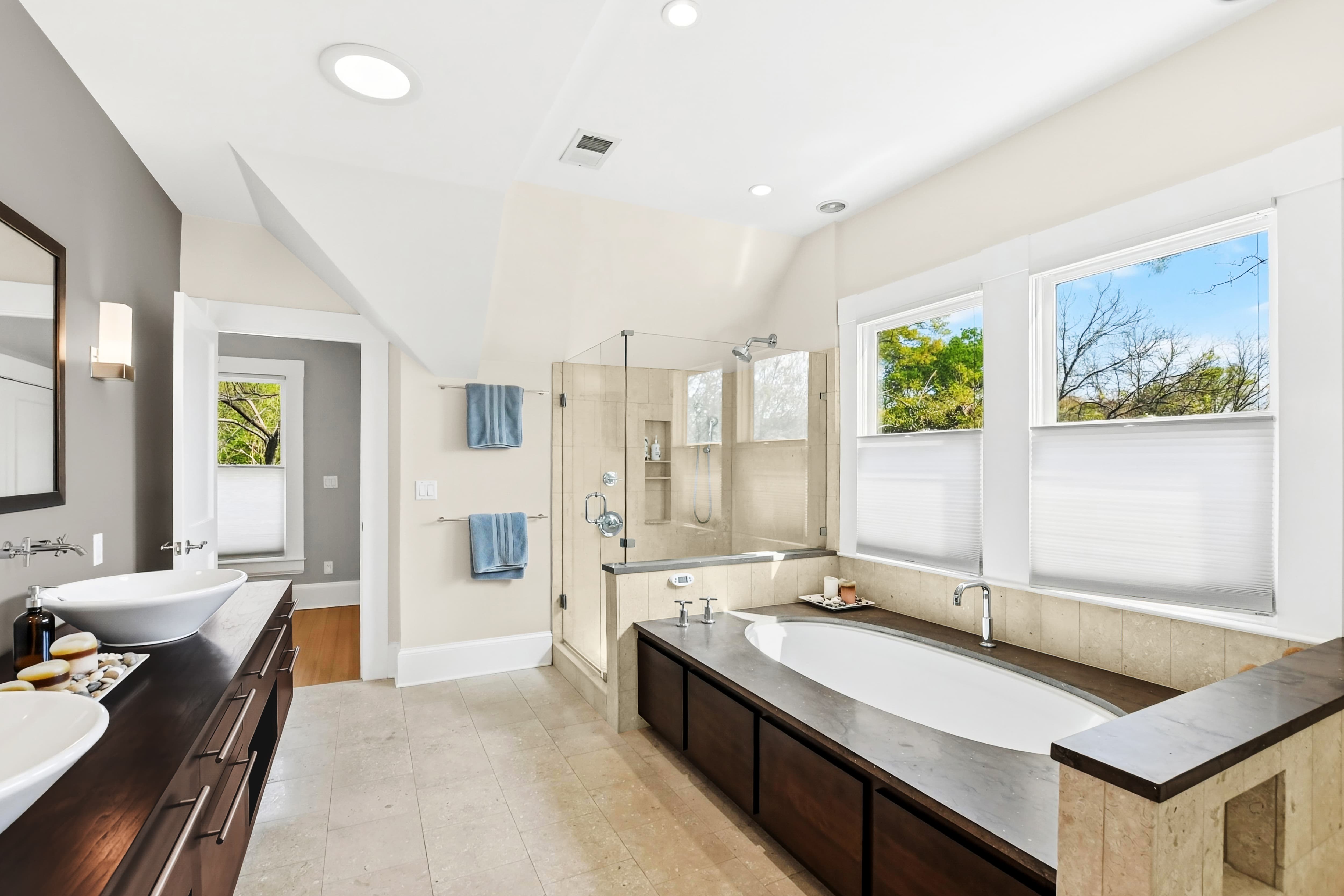 Primary bathroom with soaking tub, frameless glass shower, stone tile floors, and double vessel-sink vanity
