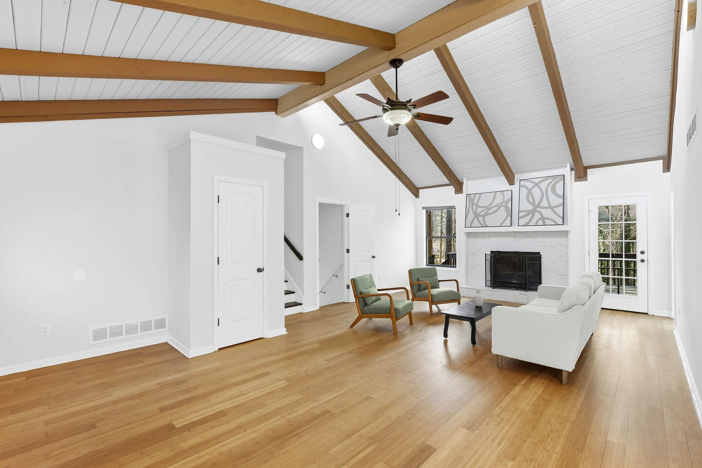 Living room with vaulted plank ceiling, exposed wood beams, white stone fireplace, and bamboo floors