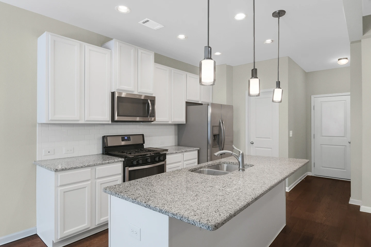 Professional HDR photograph of a kitchen focusing on granite countertops, white cabinets, and a tiled backsplash.