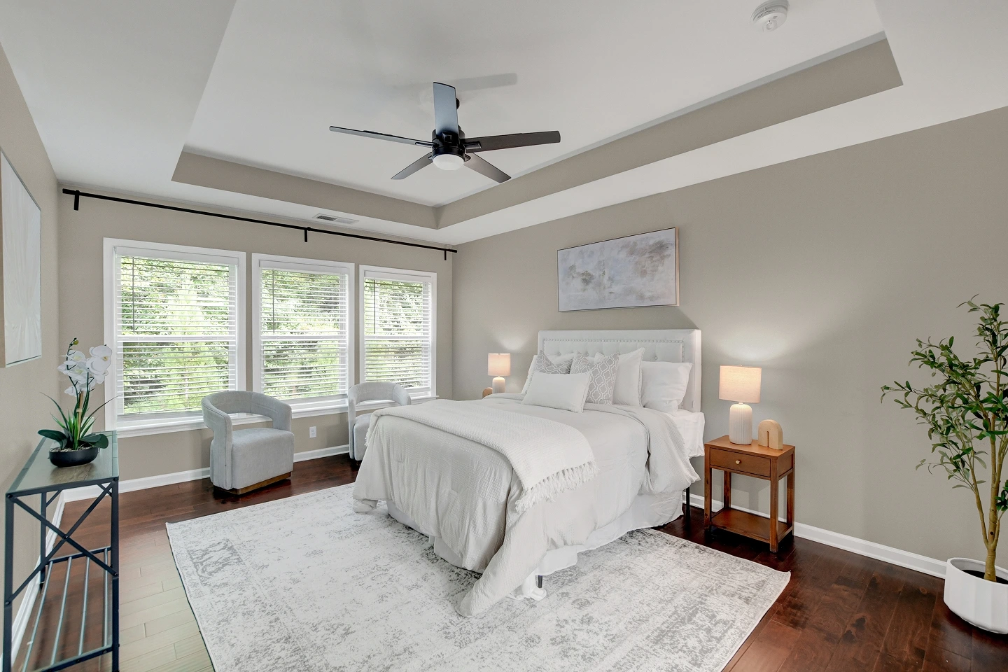 Staged primary bedroom with light walls and a vaulted tray ceiling, featuring ample natural light.
