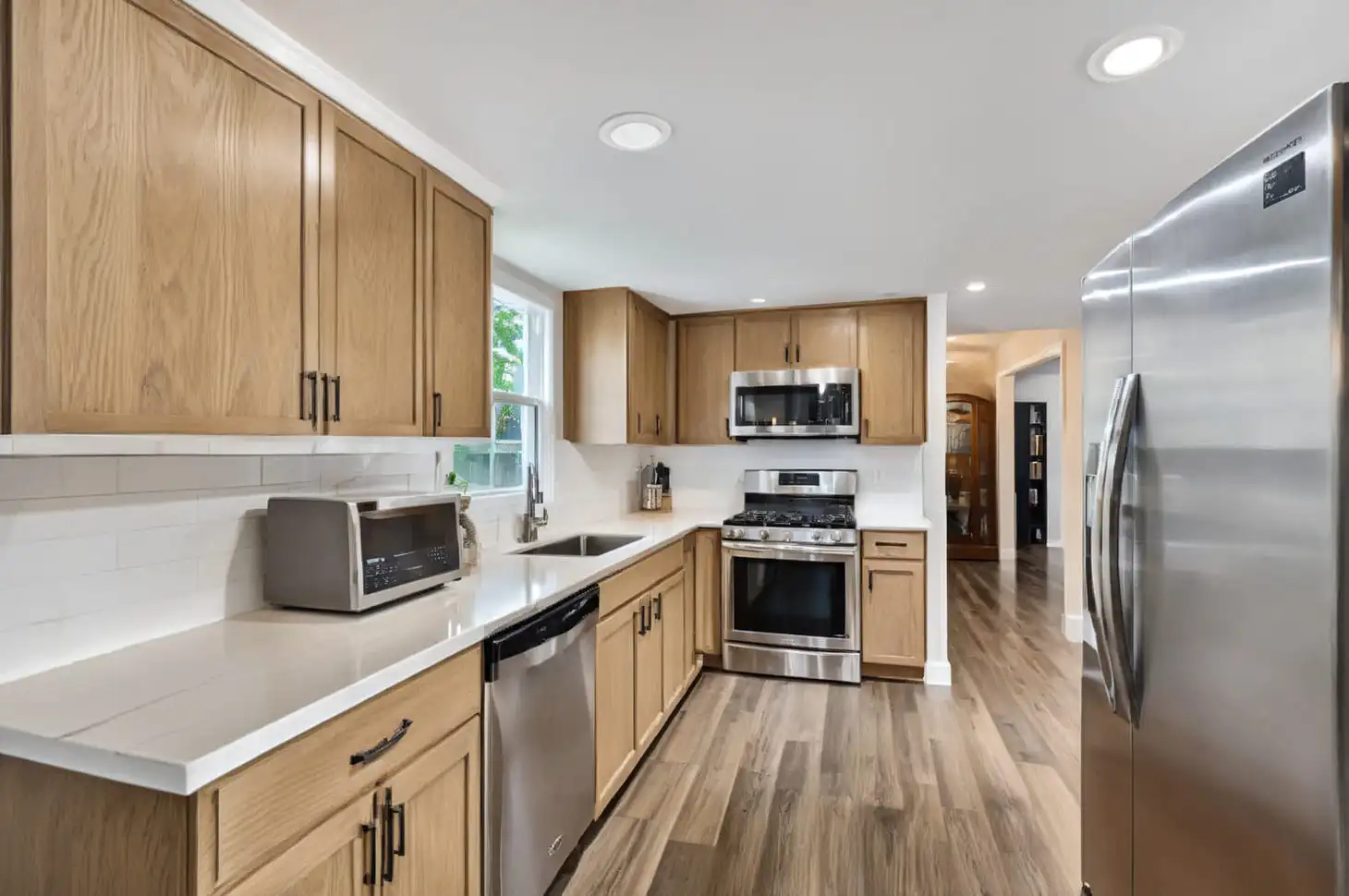 Close-up of a contemporary kitchen with light wood cabinets, stainless steel appliances, and gray countertops, showing the before version prior to AI enhancement.