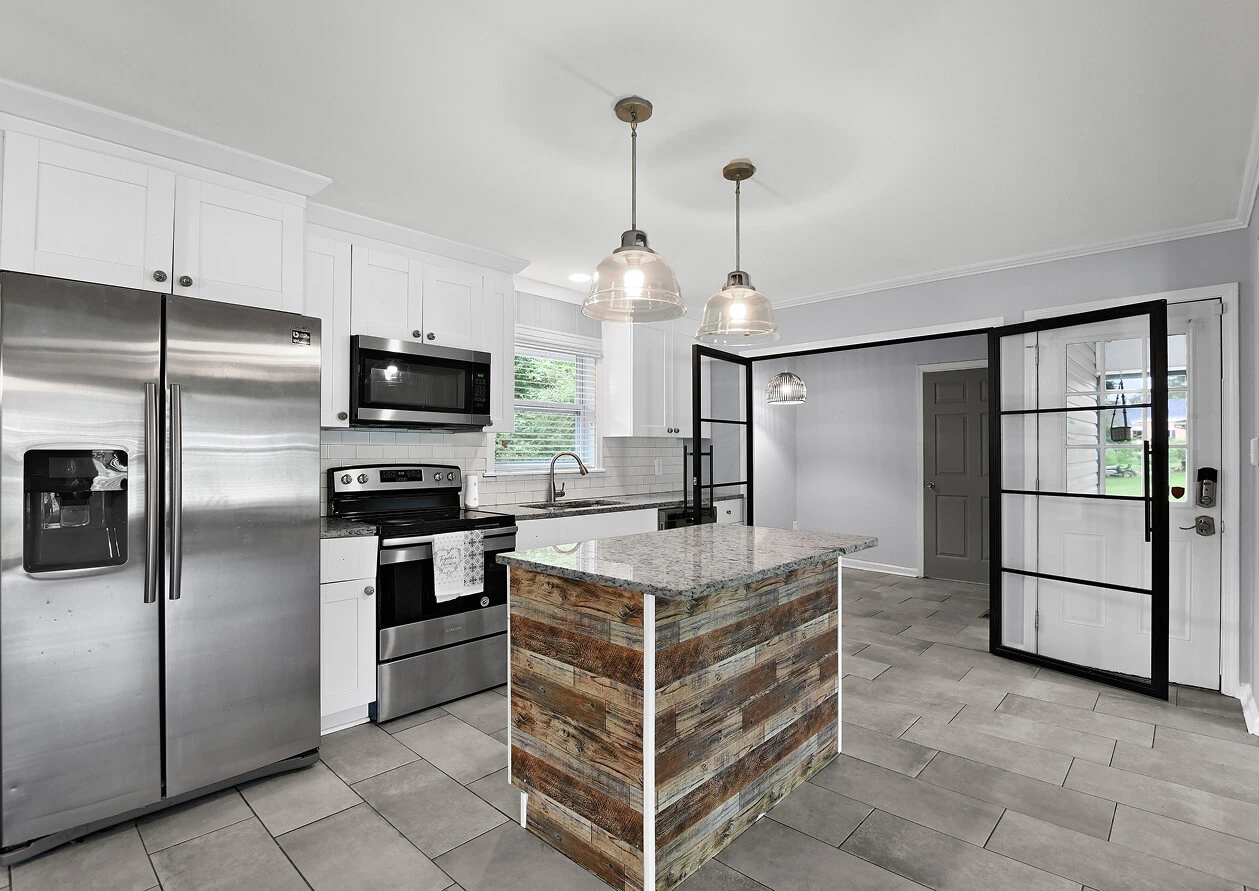 Modern kitchen with a large dark wood island, white countertops, stainless steel appliances, and pendant lighting, photographed for a real estate listing.