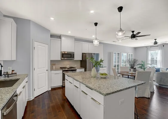 Professionally staged modern kitchen featuring white cabinetry, light countertops, a large gray island, and elegant pendant lighting.