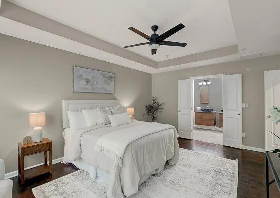 Staged primary bedroom with a large bed, light-colored walls, and a ceiling fan, creating a bright, move-in-ready appearance.